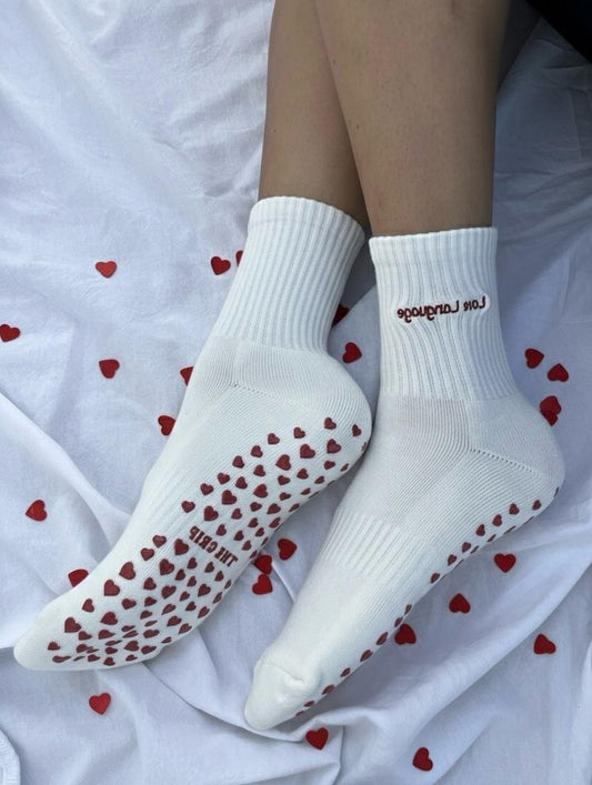 White socks with red heart patterns on a white background with red heart shapes grips.