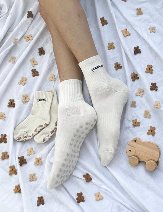 Cream white socks with grips sole on a white surface with teddy bear toys.