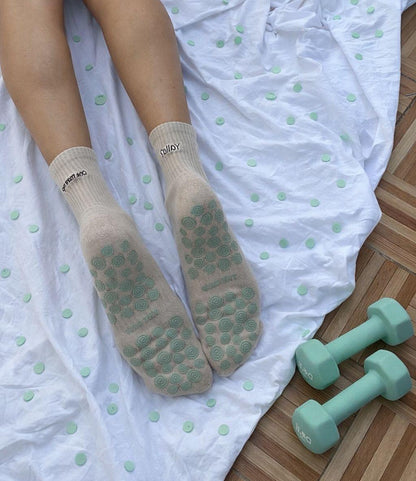 Person wearing beige socks with turquiose textured grips on the sole on a white polka dot blanket with turquiose dumbbells.