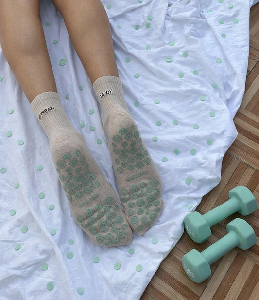 Person wearing beige socks with turquiose textured grips on the sole on a white polka dot blanket with turquiose dumbbells.