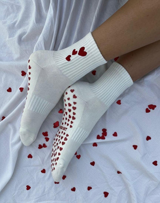 White socks with red heart patterns on a white background with red heart shapes grips.