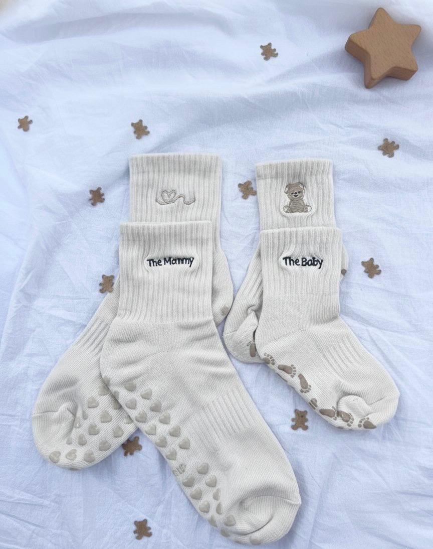 Pair of cream white socks with 'The Mommy' and 'The Baby' text on a light background with star decorations.
