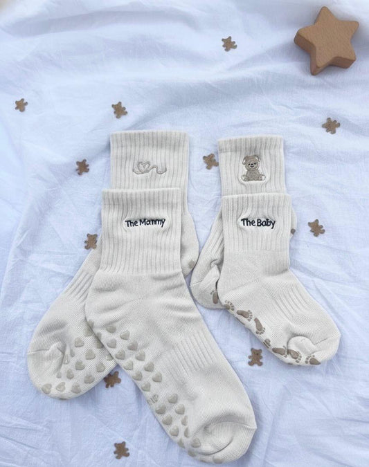 Pair of cream white socks with 'The Mommy' and 'The Baby' text on a light background with star decorations.