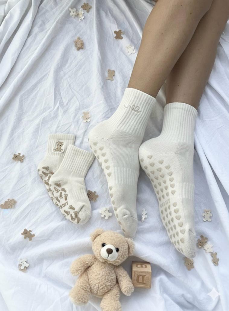 Cream white socks with textured sole on a white surface with a teddy bear and wooden blocks.